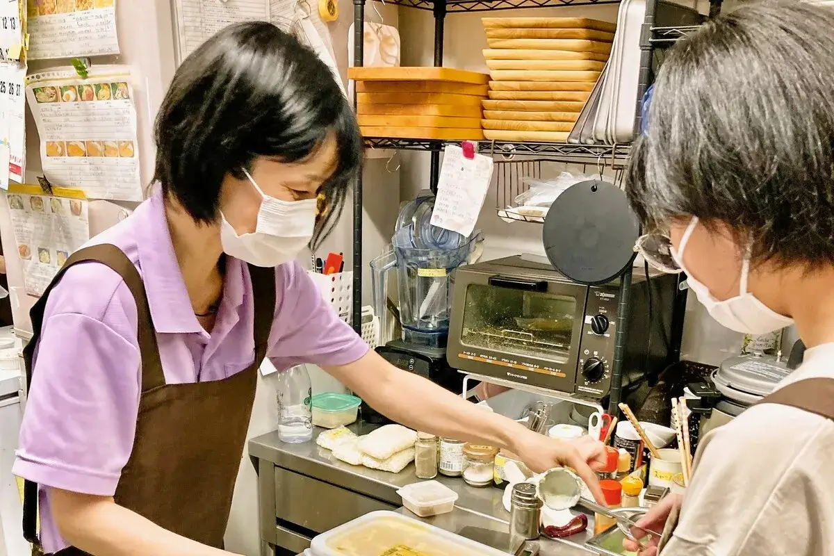 マスクを着用した2人がキッチンで調理作業をしている様子。1人は、ひきこもり当事者で、もう1人は、ワンぽてぃとのスタッフ（小栗加奈）