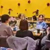 黄色い壁の飲食店で円卓を囲み、交流する女性たちのグループ。テーブルには飲み物や軽食が並んでいる。