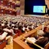 三重県民生委員・児童委員大会の講演会場。1000人以上の聴衆が、スクリーンと壇上の講演者を見ている様子。