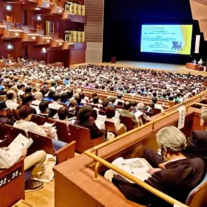 三重県民生委員・児童委員大会の講演会場。1000人以上の聴衆が、スクリーンと壇上の講演者を見ている様子。