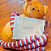 看板犬オリバーへの誕生日プレゼント。首にストライプのマフラーを巻いた茶色いくまのぬいぐるみと、「オリバーくん」と書かれたメッセージカード。