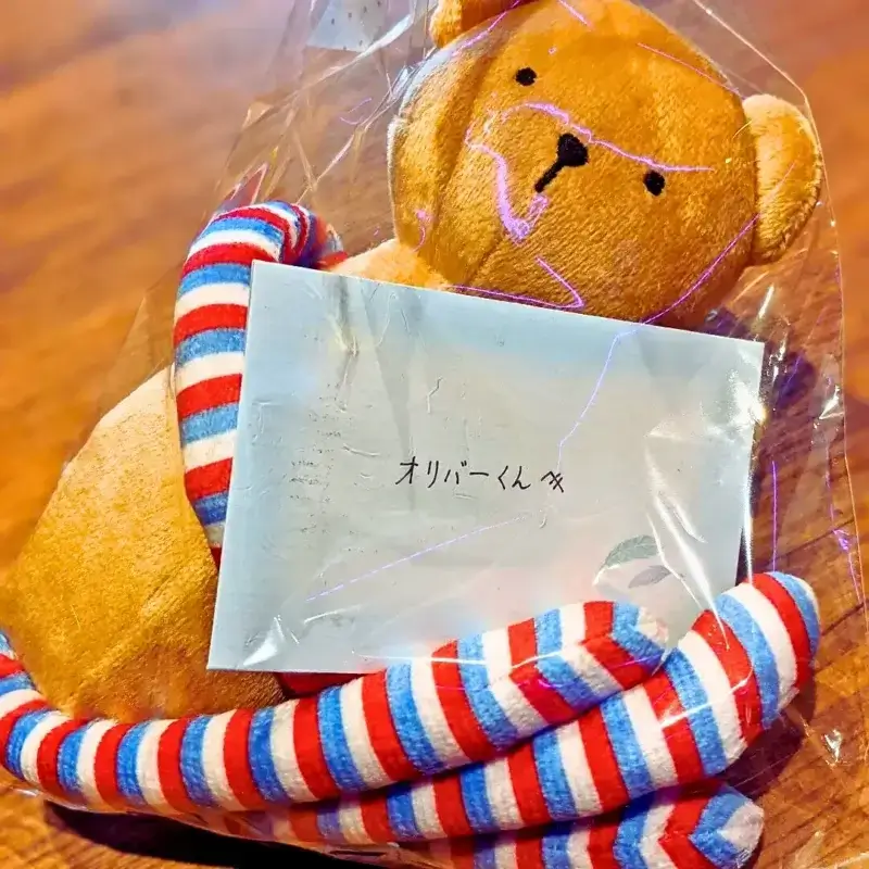 看板犬オリバーへの誕生日プレゼント。首にストライプのマフラーを巻いた茶色いくまのぬいぐるみと、「オリバーくん」と書かれたメッセージカード。