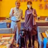 制度の狭間で苦しむ人々を救いたいと大阪から来店された男性のお客様と、ワンぽてぃとの店主、看板犬の黒いラブラドールレトリバー「ぽてぃと」の3ショット。笑顔でピースサインをする様子。