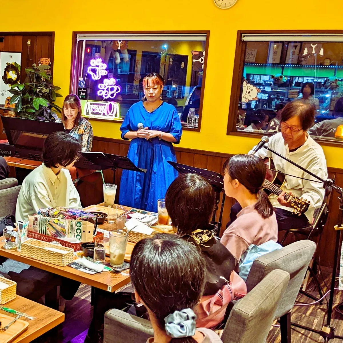 カフェレストランでのライブ演奏の様子。ボーカルとキーボード、ギターの演奏者がステージにいる。