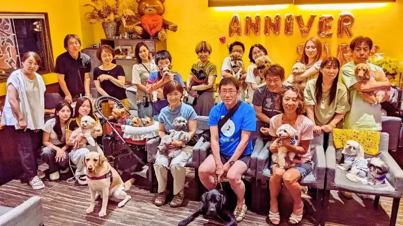 カフェレストラン「ワンぽてぃと」の店内で、たくさんの犬と飼い主さんたちが笑顔で写る「わちゃわちゃの会」アニバーサリーの集合写真。