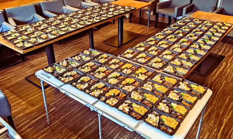 カフェのテーブルいっぱいに並べられた100食のお弁当