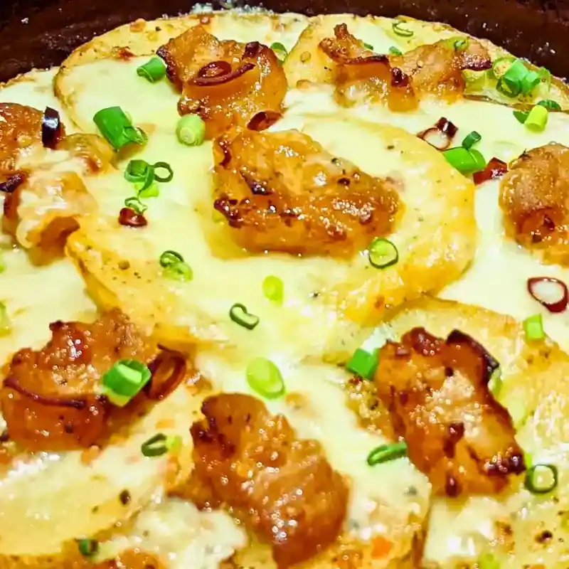 ワンぽてぃとの「牛ホルじゃがピザ」のクローズアップ画像。じゃがいもをスライスした生地の上に、とろけるチーズと香ばしく焼かれた牛ホルモン、刻みネギがたっぷり乗っている。