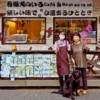 愛知県春日井市にあるカフェレストラン「ワンぽてぃと」の店先で、オーナーの小栗加奈さん（左の女性）と来店したお客様（右の女性）が、黒い看板犬と一緒にピースサインをして記念撮影している様子。