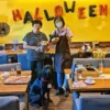 京都からのご来店に感謝|春日井カフェ「ワンぽてぃと」が目指す人との繋がり ワンぽてぃと店内でハロウィンの飾り付けを背景に、看板犬オリバーと2人の女性がぬいぐるみを持ち記念撮影している様子。
