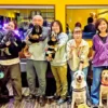 第4回「わちゃわちゃの会」の参加者と犬たちの記念撮影。黒ラブや白い大型犬、ダックスフンドなど様々な犬種が集まり、みんなで笑顔でカメラを見ている。