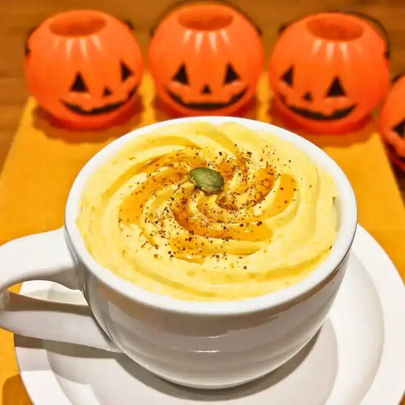 白いカップに入ったハロウィンオレ。黄色いかぼちゃクリームが渦巻き状に乗せられ、中央にパンプキンシードがトッピングされている。