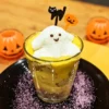 グラスに入ったかぼちゃのデザート。白いおばけのマシュマロが乗っており、背景にハロウィンの飾りが置かれている。