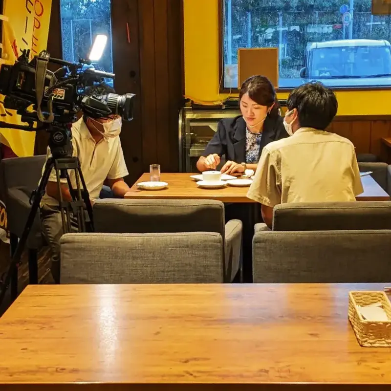 CBCテレビの取材班がワンぽてぃとで『15分雇用』についてインタビューする様子。カメラマンとスタッフ、インタビューを受ける人物がテーブルを囲んでいる。」