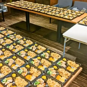 春日井市のカフェ「ワンぽてぃと」で調理された100食の手作りお弁当。就労支援（とまり木）メンバーと協力して完成させた、彩り豊かなお弁当が並んでいる様子。