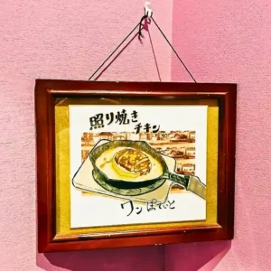 春日井市のカフェレストラン「ワンぽてぃと」のとまり木さんが描いた、本物そっくりな照り焼きチキンの手書きイラスト。店内のピンクの壁に飾られた額縁アート。