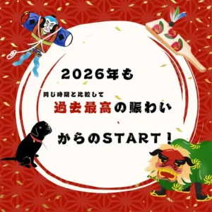 2026年の幕開けを祝う赤い和柄の背景画像。「2026年も同じ時期と比較して過去最高の賑わいからのSTART！」というテキストを中心に、凧（たこ）、羽子板、獅子舞、そして黒い犬（看板犬）のイラストが描かれている。