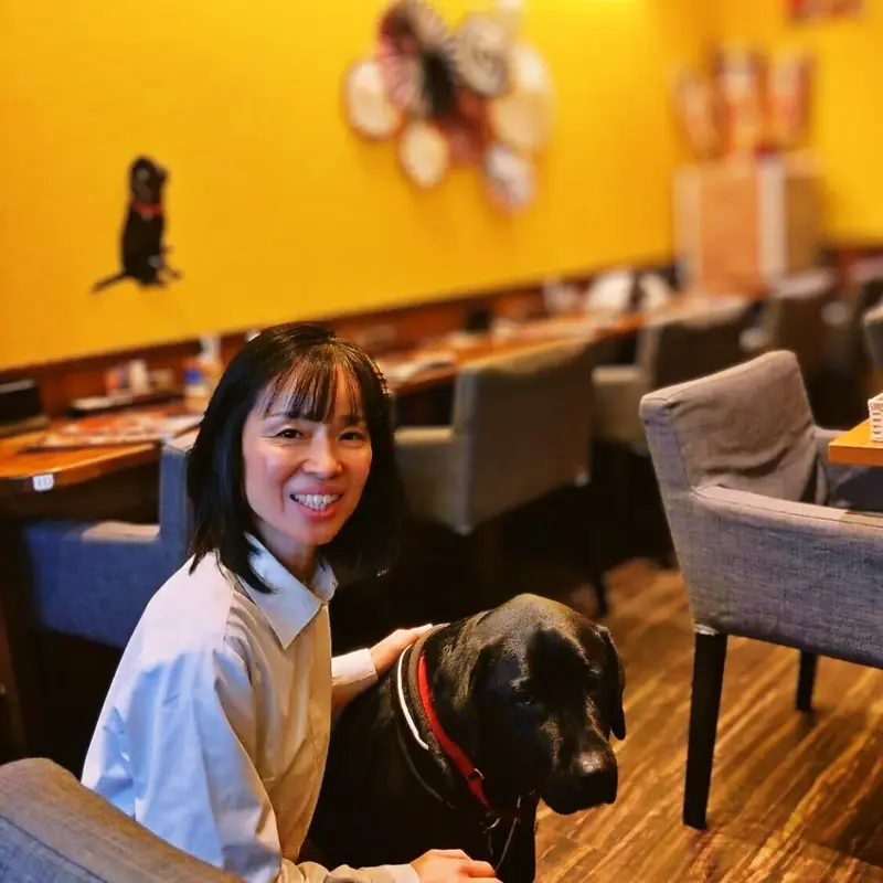 店内で看板犬の黒ラブ・オリバーに寄り添い、優しく微笑むオーナー小栗。「みんなが創りあげてくれた場所 それが、ワンぽてぃとなのです」というメッセージ。