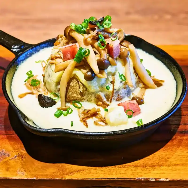 熱々のスキレットに盛られた和風じゃがグラ。たっぷりのきのことベーコン、青ネギがトッピングされ、焦がし醤油の香ばしさが漂う。