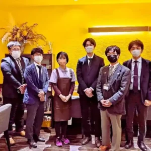 愛知県春日井市のカフェレストラン「ワンぽてぃと」にて、視察に訪れた東北地方の自治体職員の方々と小栗加奈代表が並んで笑顔で記念撮影している様子