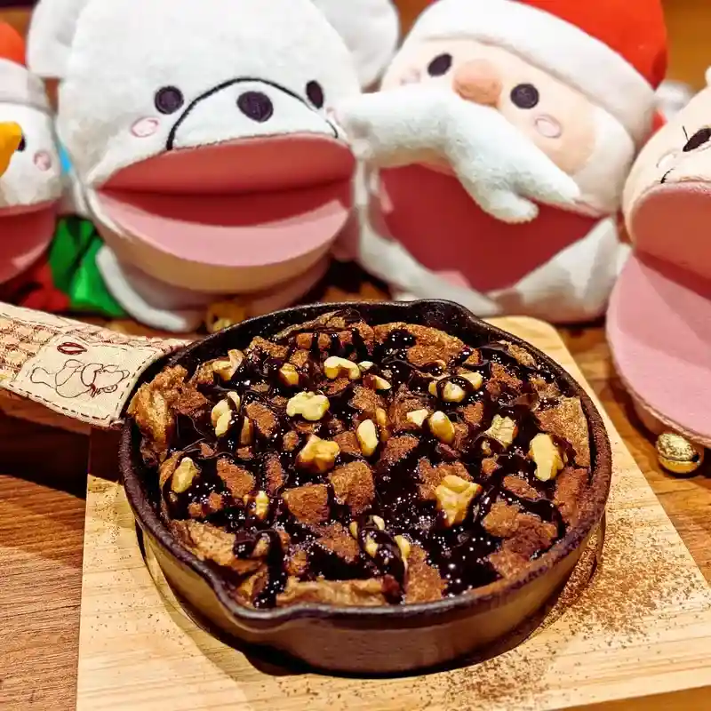 熱々のスキレットで焼き上げられたチョコレートパンプディング。たっぷりのチョコソースとカリッとした胡桃がトッピングされている。