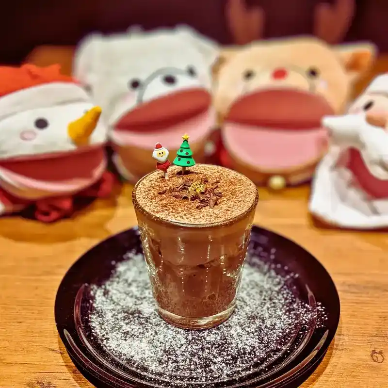 ガラスの器に入った濃厚なチョコレートトライフル。上には削りチョコと金粉、小さなサンタとツリーのピックが飾られている。