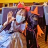 ハロウィンの魔女の帽子とマントをつけた黒ラブラドールの看板犬オリバーと、赤いリボンをつけ白いエプロンドレスを着たオーナーの小栗加奈が笑顔で並んでいる写真。