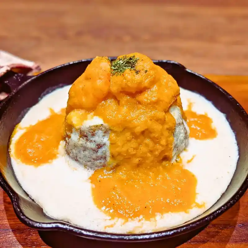スキレットに盛り付けられたホクホクのじゃがいもに、濃厚なオレンジ色のアメリケーヌソースとホワイトソースがかかったアメリケーヌじゃがグラ