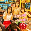 春日井市のカフェ・ワンぽてぃとで、看板犬の黒ラブ・オリバーと笑顔の女性ボランティアたちが「温かい絆 広がる縁」という文字と共に談笑している様子