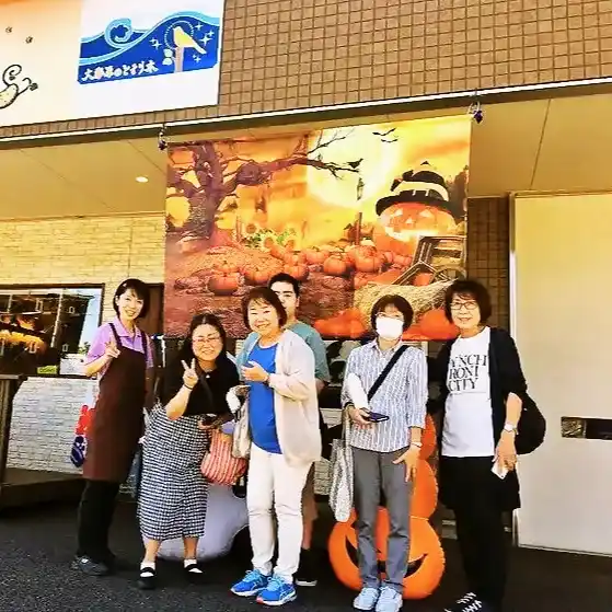「大人の寺子屋 とまり木」の看板の前で、ハロウィンの飾り付けを背景に笑顔で並ぶスタッフと参加者の集合写真