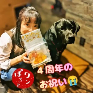 4周年のお祝いでいただいた看板犬オリバーそっくりの飴細工を持つオーナーと、隣に並ぶ黒ラブのオリバー