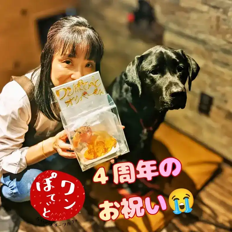 4周年のお祝いでいただいた看板犬オリバーそっくりの飴細工を持つオーナーと、隣に並ぶ黒ラブのオリバー