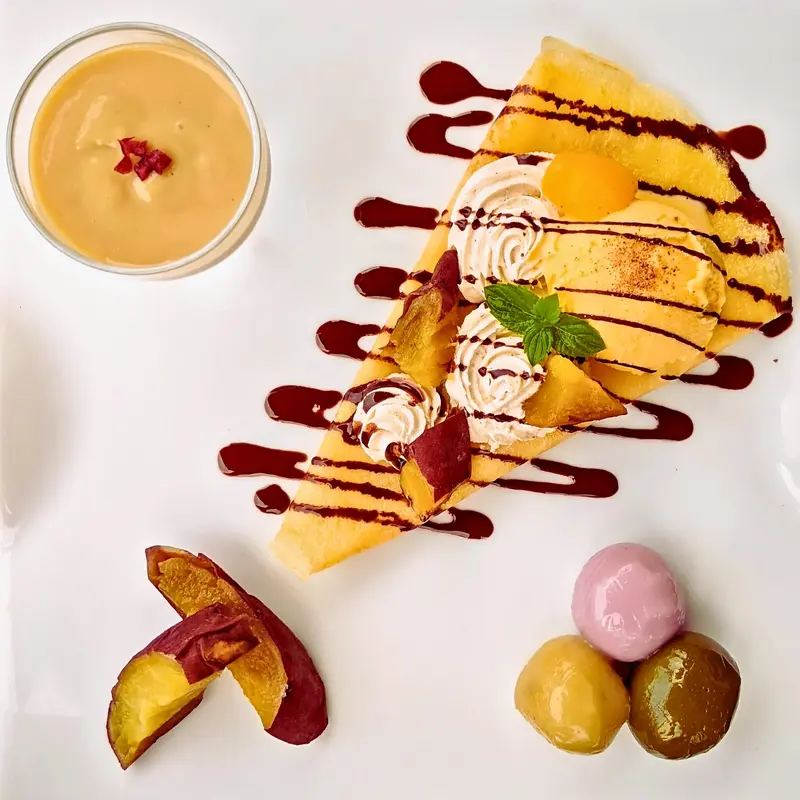 白いプレートに華やかに盛り付けられた「ワンぽてぃと SWEETS PLATE」。中央にはチョコソースがけのクレープ(生クリーム、さつまいもアイス、マロングラッセ、角切りおいも、ミント添え)があり、左上にクランベリーがのった蜜芋プリンのグラス、左下に2種類の焼き芋(女いも・男いも)、右下に3色のお団子(紫いも・抹茶・さつまいも)が添えられている。