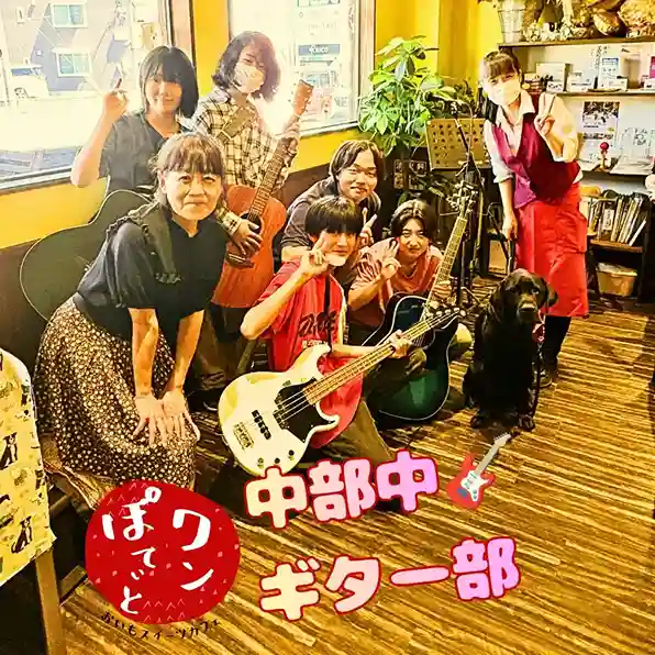 春日井市のカフェレストラン「ワンぽてぃと」店内でオーナーの小栗加奈、看板犬オリバー、中部中学校ギター部の顧問と生徒が楽器を持って笑顔で並ぶ集合写真