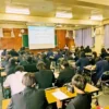 満員の名古屋北高校の教室で、カフェ「ワンぽてぃと」オーナーの小栗加奈による15分雇用や不登校・ひきこもり支援（とまり木事業）の講演に真剣に耳を傾け、メモを取る高校生たちの後ろ姿