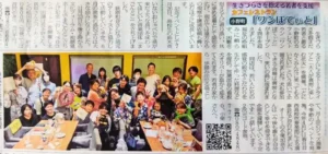 生きづらさを抱える若者を支援するカフェレストラン「ワンぽてぃと」の新聞記事。オーナーの小栗加奈さんや看板犬のオリバーについての記載と、イベントに集まった大勢の人々の笑顔の集合写真が掲載されています。