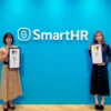 SmartHRのロゴを背景に、WORK DESIGN AWARD 2023のグランプリ受賞盾を持つワンぽてぃとオーナーの小栗加奈と娘